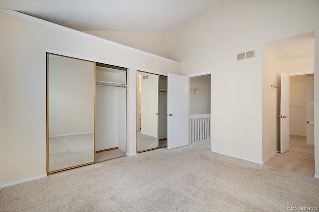 unfurnished bedroom with two closets, light colored carpet, and high vaulted ceiling