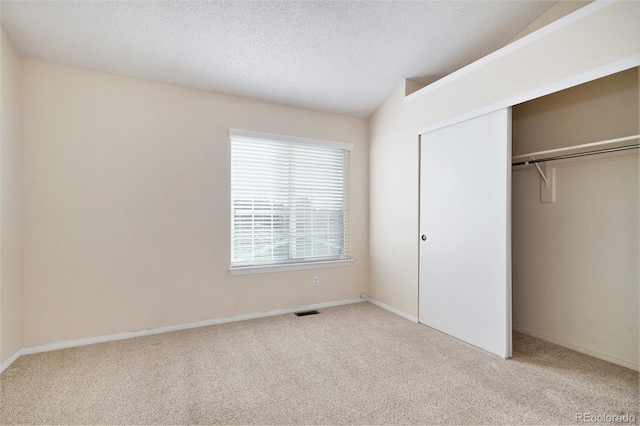 unfurnished bedroom featuring light carpet, a textured ceiling, vaulted ceiling, and a closet