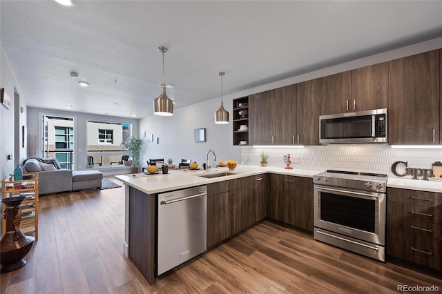 kitchen featuring dark wood-type flooring, sink, appliances with stainless steel finishes, kitchen peninsula, and backsplash