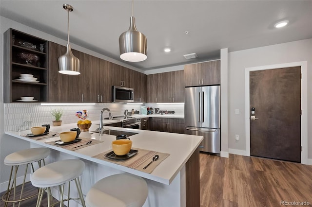 kitchen featuring appliances with stainless steel finishes, a kitchen breakfast bar, hanging light fixtures, kitchen peninsula, and dark brown cabinets