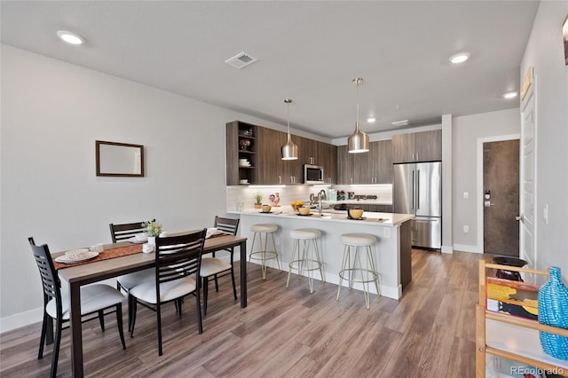 kitchen featuring pendant lighting, stainless steel appliances, dark brown cabinetry, tasteful backsplash, and kitchen peninsula