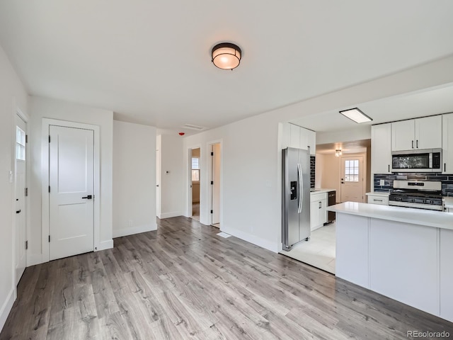 kitchen with light wood-type flooring, white cabinets, stainless steel appliances, and decorative backsplash