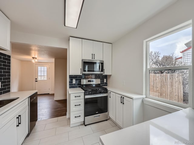 kitchen featuring light wood-type flooring, backsplash, stainless steel appliances, and white cabinetry