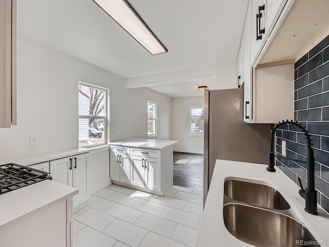 kitchen with tasteful backsplash, kitchen peninsula, sink, and white cabinets