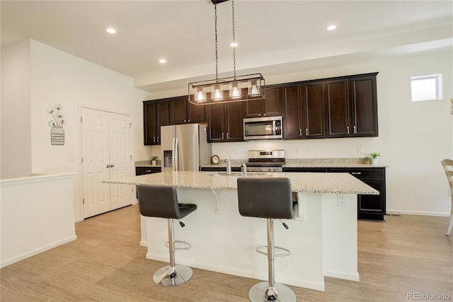 6717 Golden Briar Ln, Colorado Springs, CO 80927 - kitchen featuring appliances with stainless steel finishes, a breakfast bar, a center island with sink, light wood-type flooring, and dark brown cabinetry