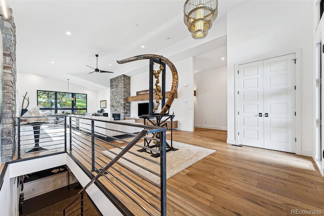 interior space featuring ceiling fan with notable chandelier, a stone fireplace, vaulted ceiling, and hardwood / wood-style floors