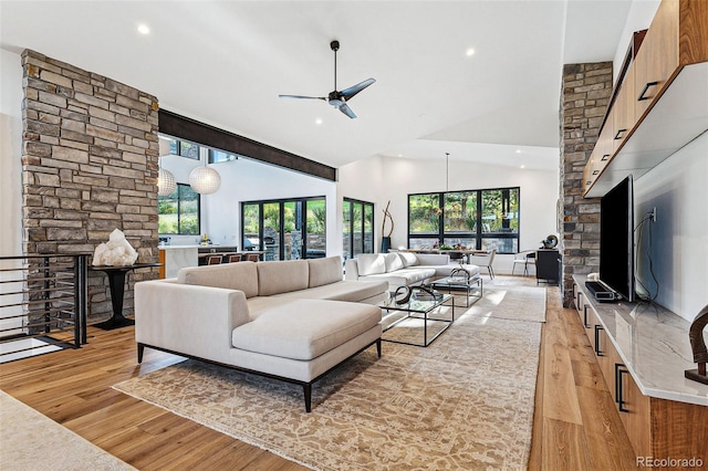 living room featuring ceiling fan, a stone fireplace, light wood-type flooring, and high vaulted ceiling