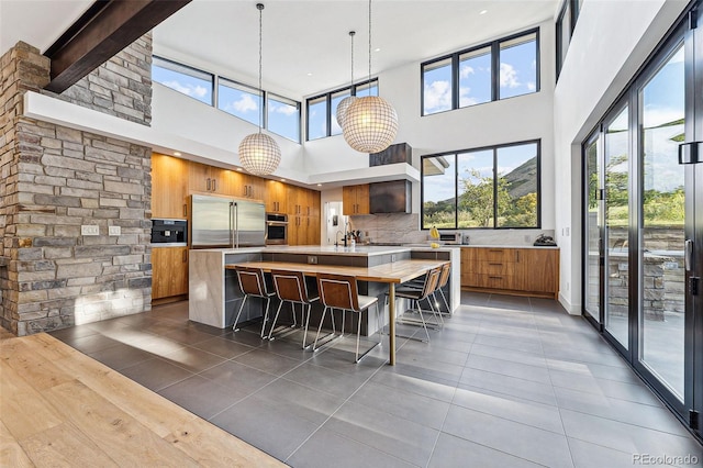 kitchen featuring pendant lighting, a kitchen island with sink, tasteful backsplash, a kitchen bar, and a high ceiling