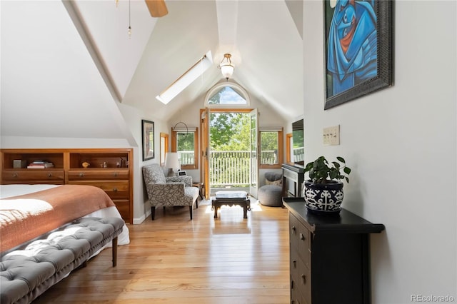bedroom with access to exterior, light wood-style floors, a skylight, and high vaulted ceiling