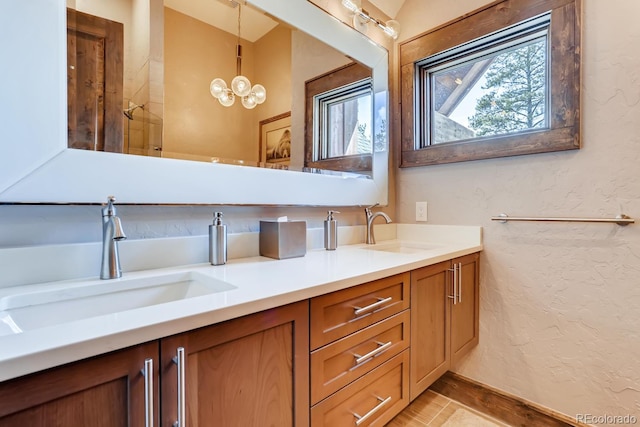 full bath with a textured wall, double vanity, a sink, and an inviting chandelier