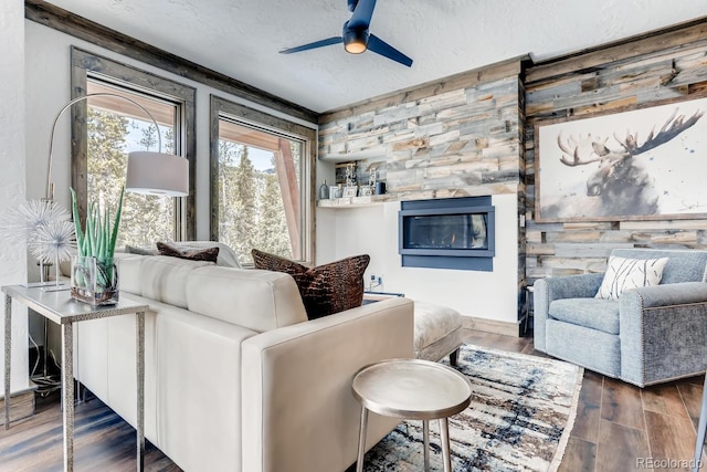 living area featuring ceiling fan, dark wood-type flooring, a textured ceiling, and a glass covered fireplace