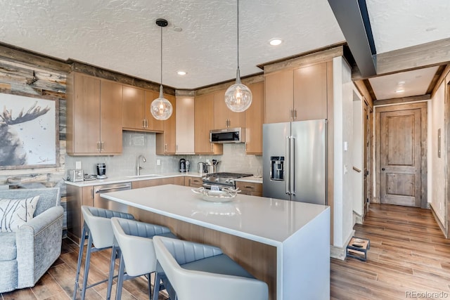 kitchen featuring premium appliances, decorative light fixtures, light countertops, light wood-style floors, and a sink