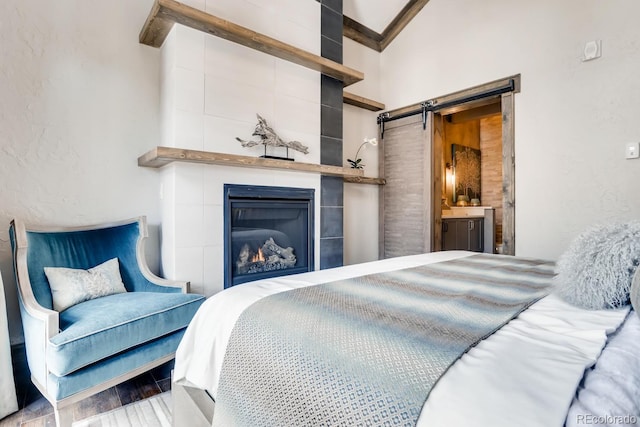 bedroom with ensuite bathroom, a textured wall, a barn door, a large fireplace, and wood finished floors