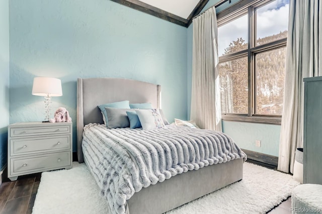 bedroom featuring lofted ceiling, a textured wall, and multiple windows