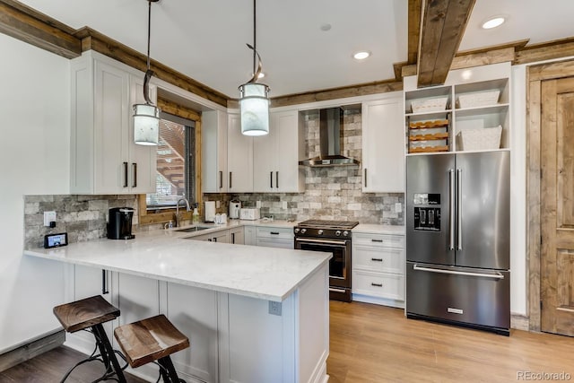 kitchen with a sink, white cabinetry, hanging light fixtures, wall chimney range hood, and high end appliances