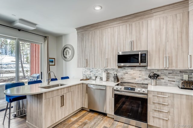 kitchen with a breakfast bar, light countertops, light brown cabinetry, appliances with stainless steel finishes, and a peninsula