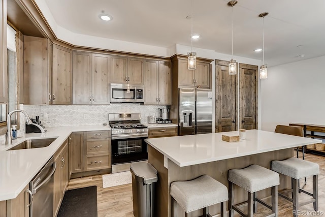 kitchen with a kitchen island, a sink, light countertops, appliances with stainless steel finishes, and decorative light fixtures