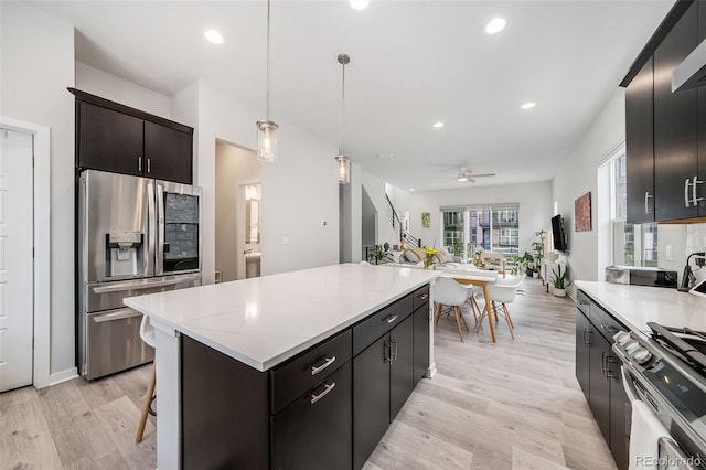kitchen featuring a ceiling fan, appliances with stainless steel finishes, a center island, open floor plan, and light wood-style floors