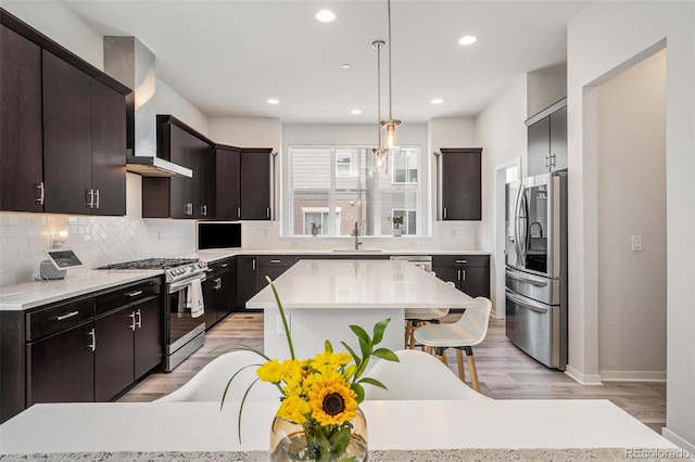 kitchen with decorative backsplash, appliances with stainless steel finishes, a sink, light countertops, and wall chimney exhaust hood