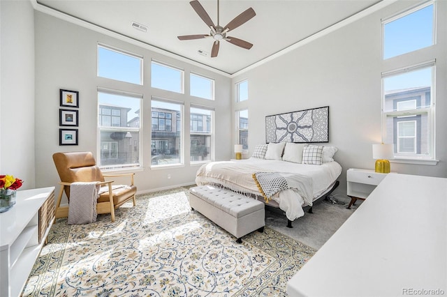 carpeted bedroom with crown molding, a high ceiling, visible vents, and ceiling fan