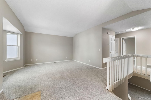 unfurnished room with carpet flooring, lofted ceiling, and a textured ceiling