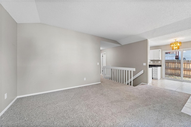 spare room with a chandelier, lofted ceiling, a textured ceiling, and light colored carpet