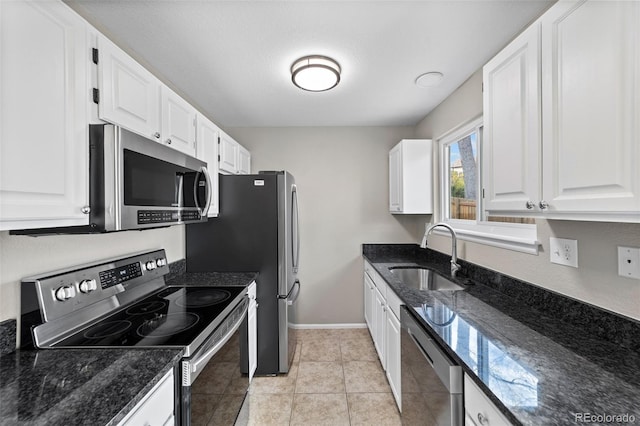 kitchen with sink, appliances with stainless steel finishes, dark stone countertops, light tile patterned floors, and white cabinets