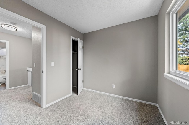 unfurnished bedroom with a textured ceiling, light colored carpet, and multiple windows