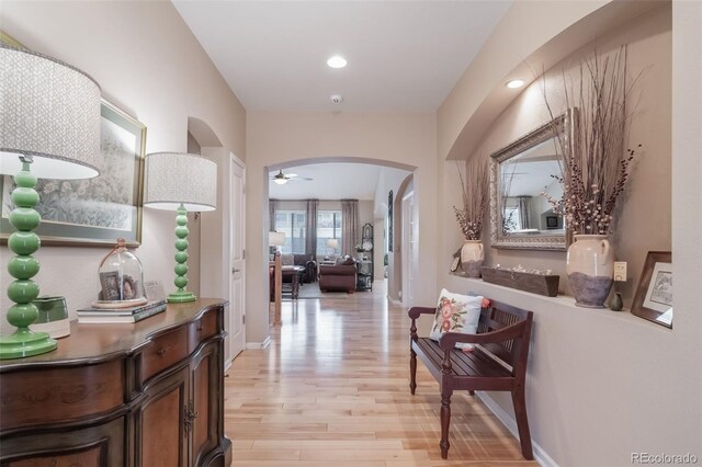 corridor with light wood-style floors, arched walkways, baseboards, and recessed lighting