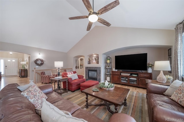 living area featuring arched walkways, ceiling fan, a glass covered fireplace, and light wood-style floors