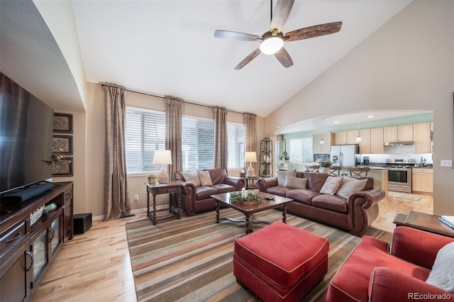 living room featuring ceiling fan, arched walkways, light wood-type flooring, high vaulted ceiling, and baseboards