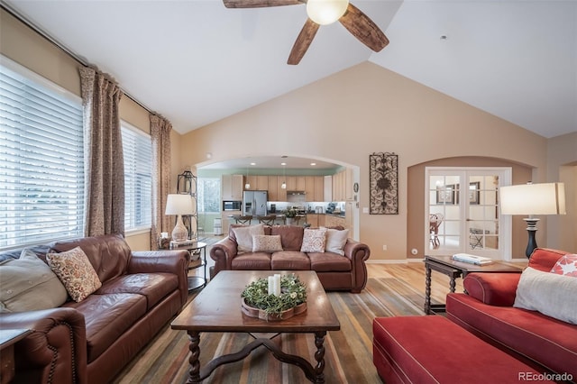 living room featuring baseboards, ceiling fan, high vaulted ceiling, light wood-type flooring, and arched walkways