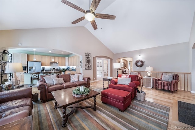 living room with arched walkways, a ceiling fan, high vaulted ceiling, and light wood-style floors