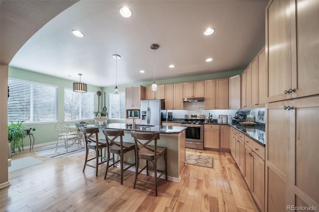 kitchen featuring light brown cabinetry, baseboards, a breakfast bar area, under cabinet range hood, and stainless steel appliances