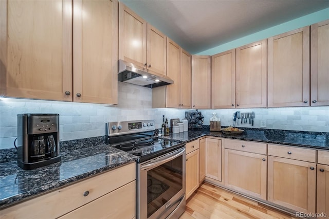 kitchen with light brown cabinets, dark stone countertops, under cabinet range hood, electric stove, and light wood finished floors