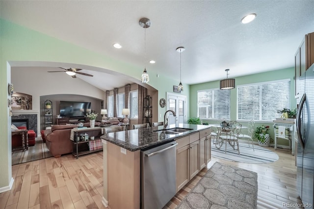 kitchen featuring appliances with stainless steel finishes, arched walkways, vaulted ceiling, a sink, and light wood finished floors