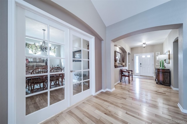 entryway featuring a chandelier, arched walkways, wood finished floors, baseboards, and lofted ceiling