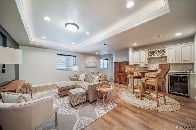 living area featuring visible vents, crown molding, wine cooler, light wood-type flooring, and a tray ceiling