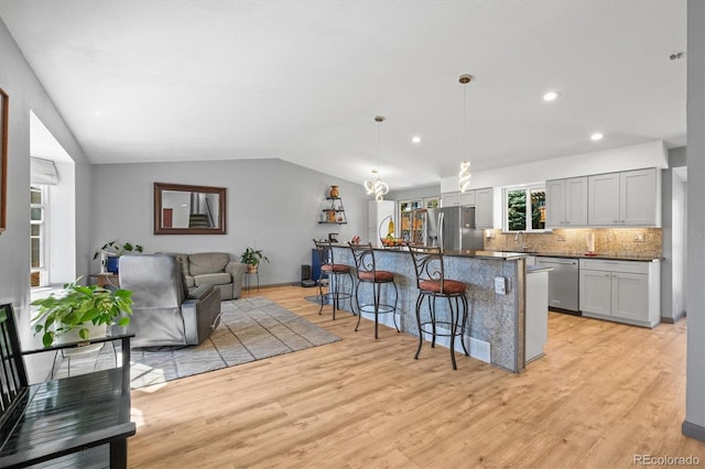 kitchen with backsplash, a breakfast bar, lofted ceiling, appliances with stainless steel finishes, and light wood-style floors