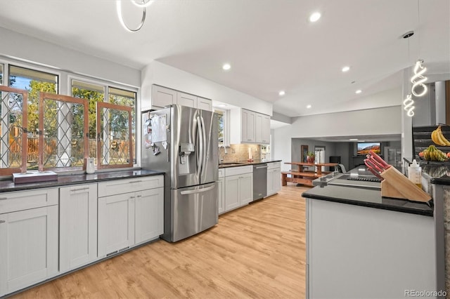 kitchen featuring dark countertops, light wood-type flooring, decorative backsplash, appliances with stainless steel finishes, and a sink