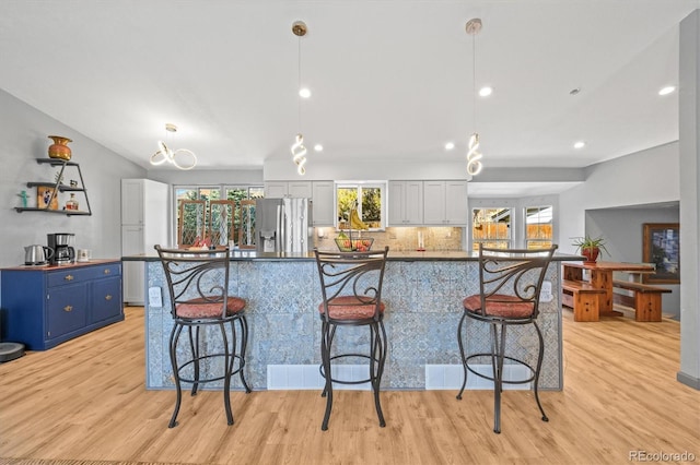 kitchen featuring a breakfast bar area, blue cabinetry, stainless steel fridge with ice dispenser, decorative backsplash, and light wood-style floors