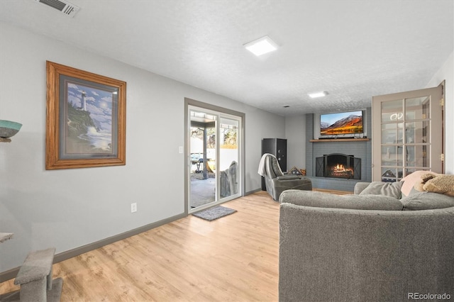 living room featuring visible vents, baseboards, a brick fireplace, and light wood finished floors