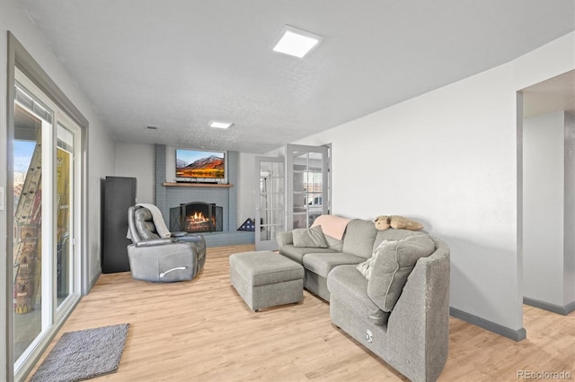 living area featuring french doors, baseboards, a brick fireplace, and light wood-style flooring