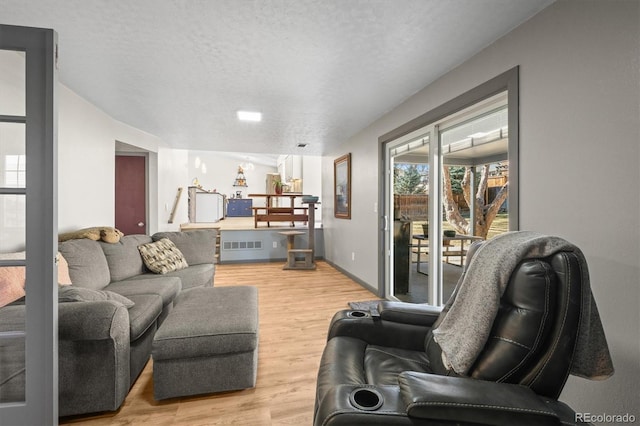 living area with visible vents, baseboards, a textured ceiling, and light wood-style flooring