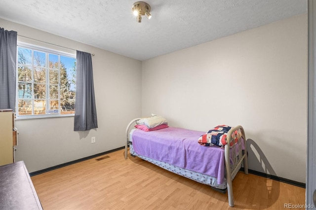 bedroom featuring a textured ceiling, wood finished floors, visible vents, and baseboards