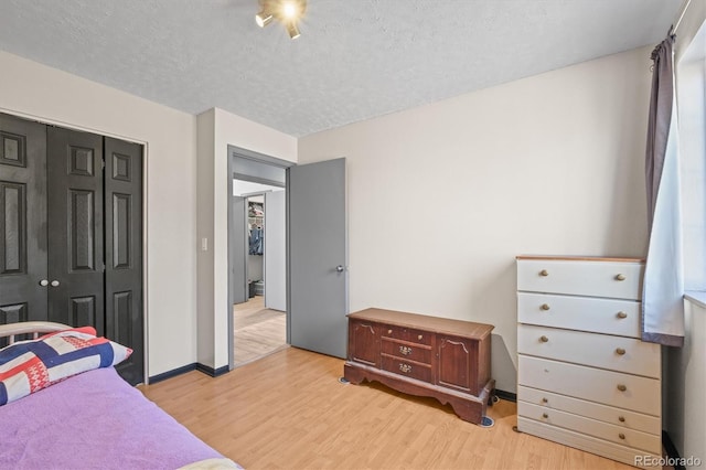 bedroom featuring a closet, baseboards, light wood-style floors, and a textured ceiling