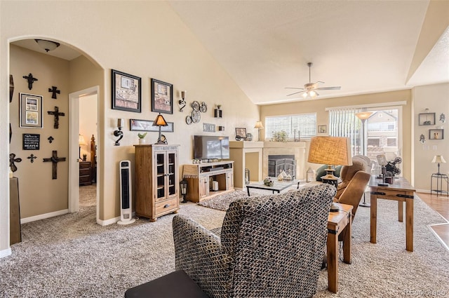 living room with ceiling fan, arched walkways, baseboards, a glass covered fireplace, and light colored carpet