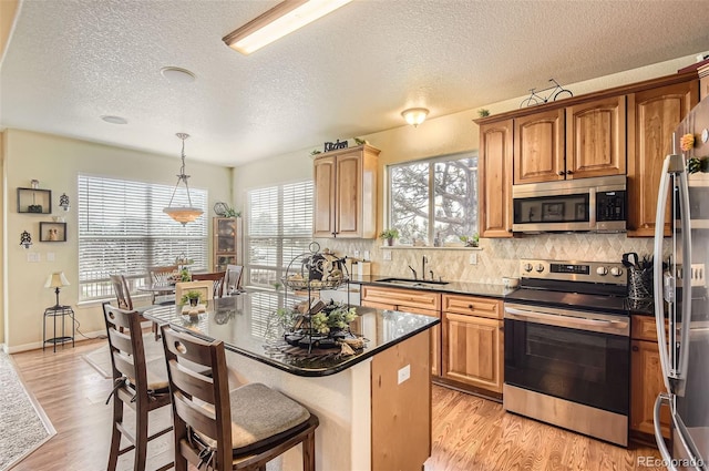 kitchen with appliances with stainless steel finishes, a sink, light wood-type flooring, backsplash, and a kitchen island