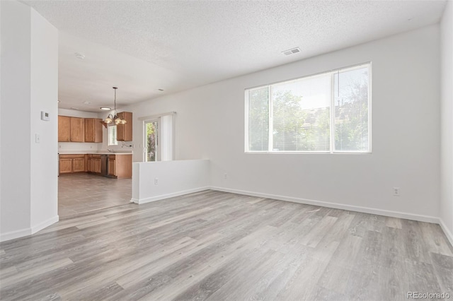 19466 E 59th Dr, Aurora, CO 80019 - unfurnished living room featuring a chandelier, light wood finished floors, plenty of natural light, and a textured ceiling