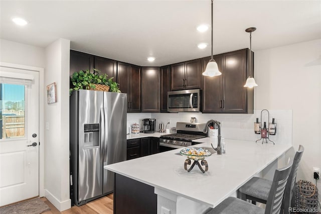 kitchen with dark brown cabinets, light countertops, a peninsula, stainless steel appliances, and light wood-style flooring